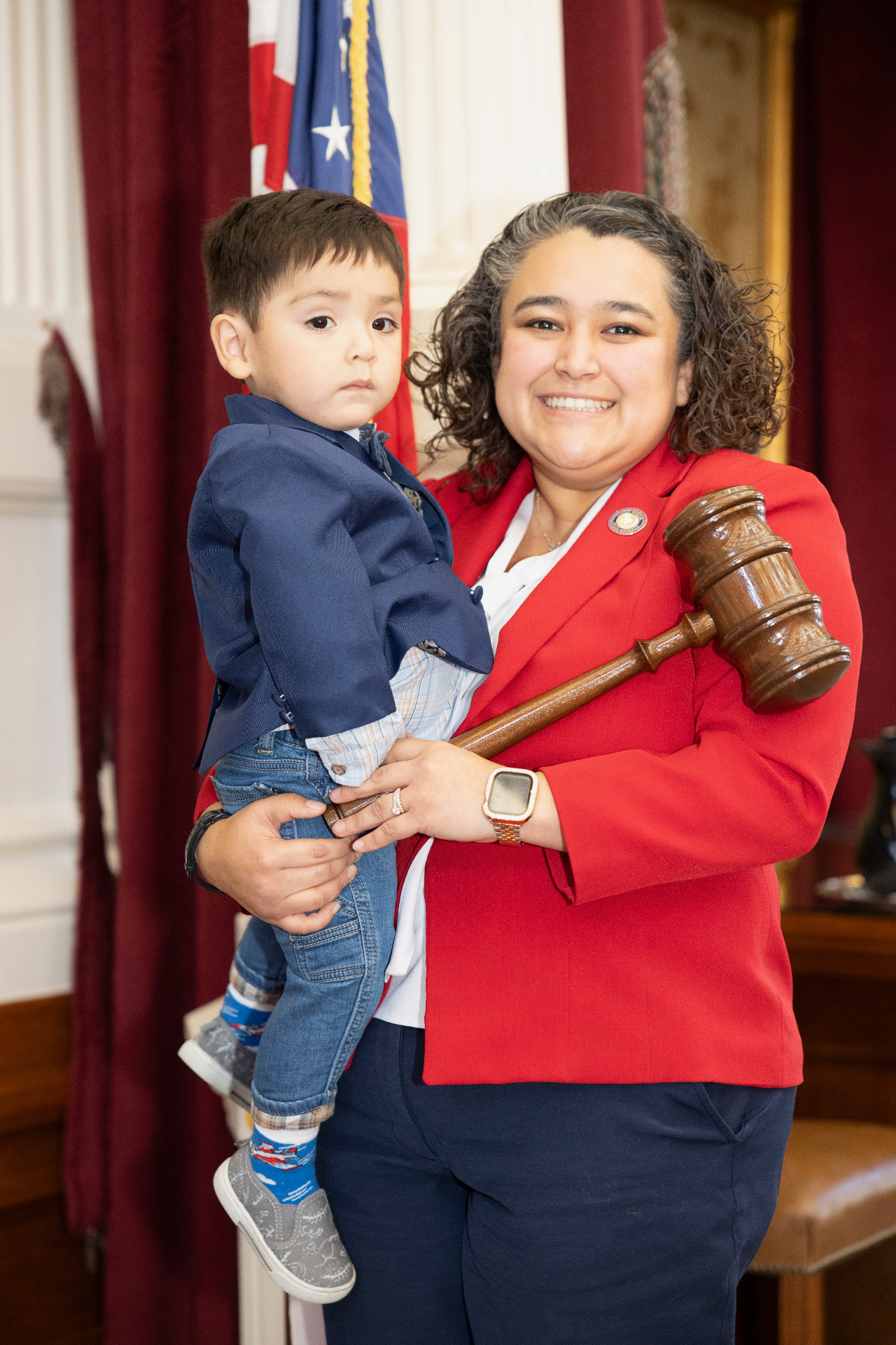 Denise in her red blazer holding her son Zeke and the Speaker's gavel.